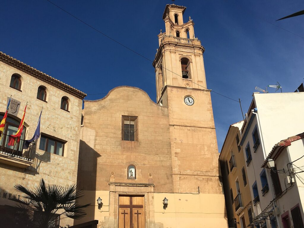 Church of Saint Bartholomew with its bell tower rising above the old town of Finestrat against a deep blue sky