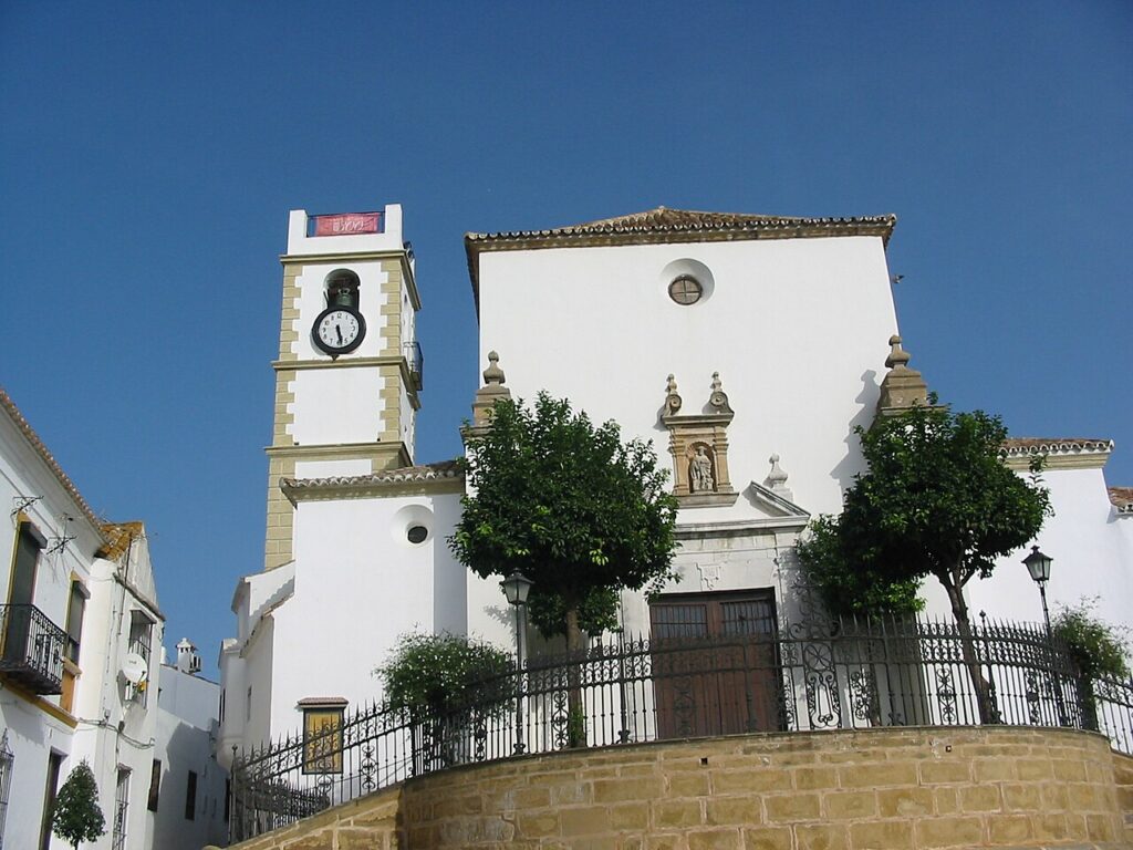 White facade and clock tower of the parish church of Santa Maria la Coronada in San Roque, Andalusia, against a blue sky
