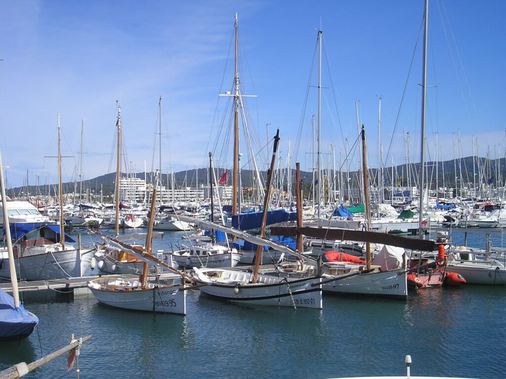Traditional llaut sailing boats and yachts moored in the harbour of Sant Antoni de Portmany, Ibiza, with hills behind