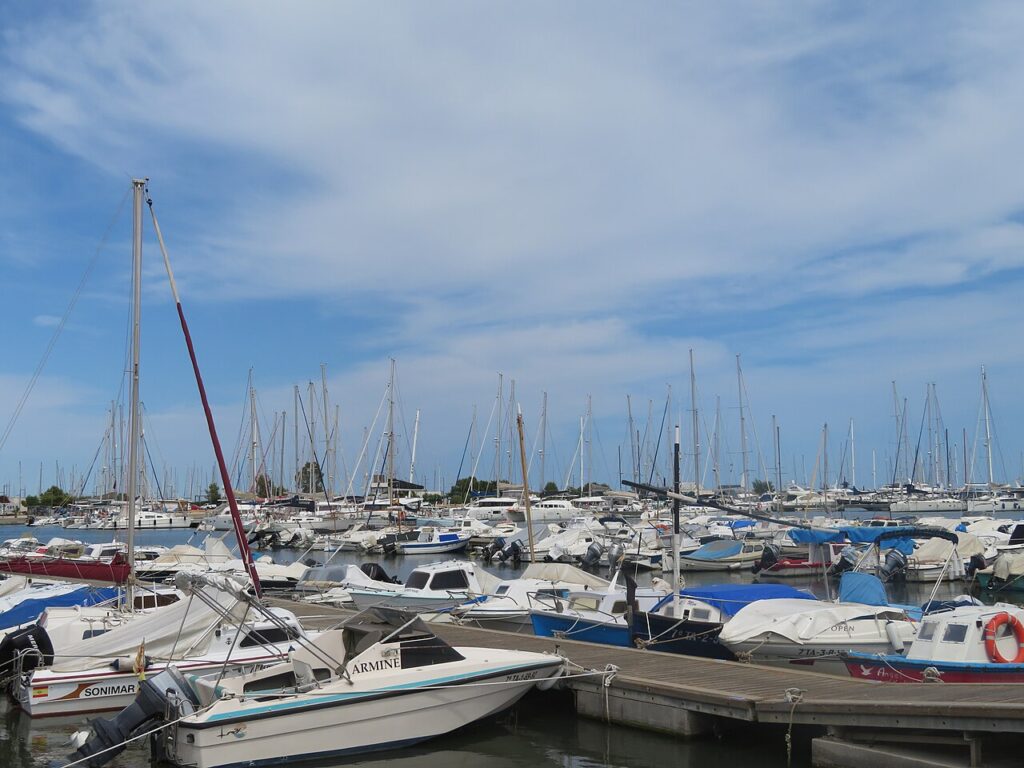 The marina of Sant Carles de la Ràpita with rows of moored sailing boats and motorboats under a partly cloudy sky