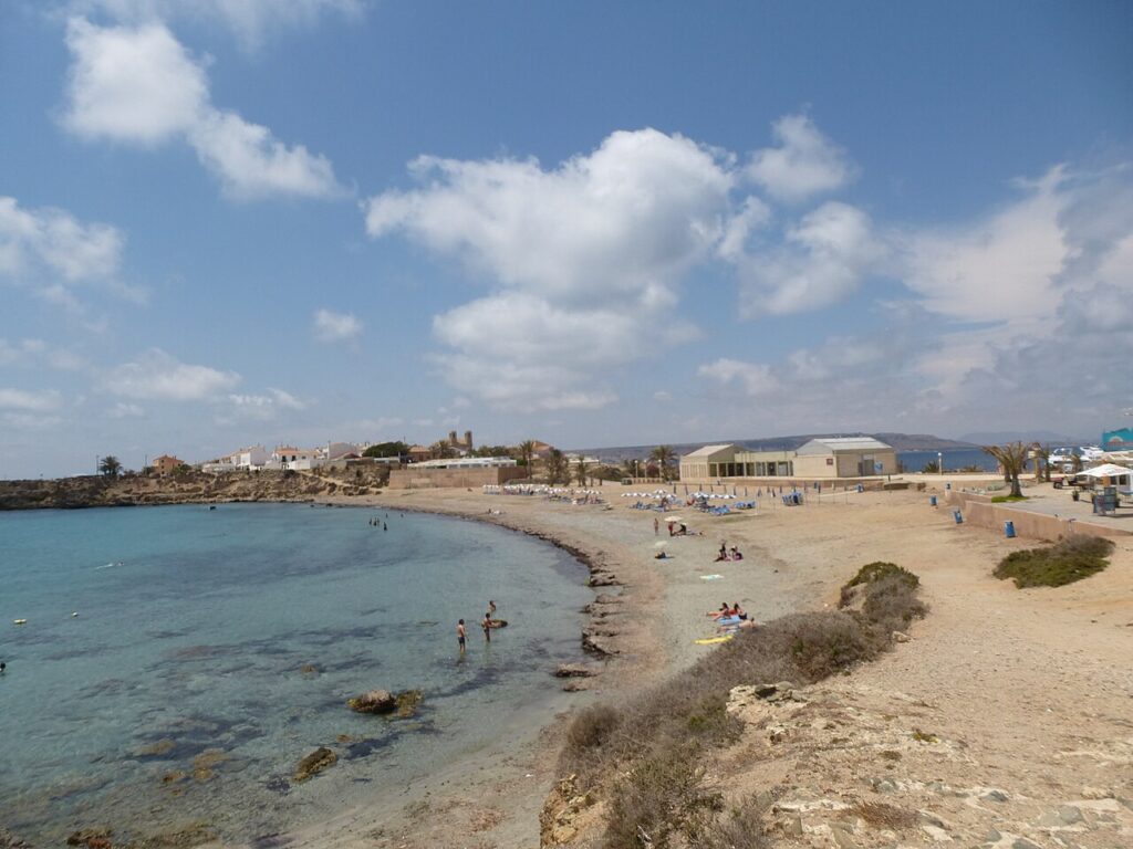 The small beach and low rocky shore of Tabarca island under a blue sky with clouds