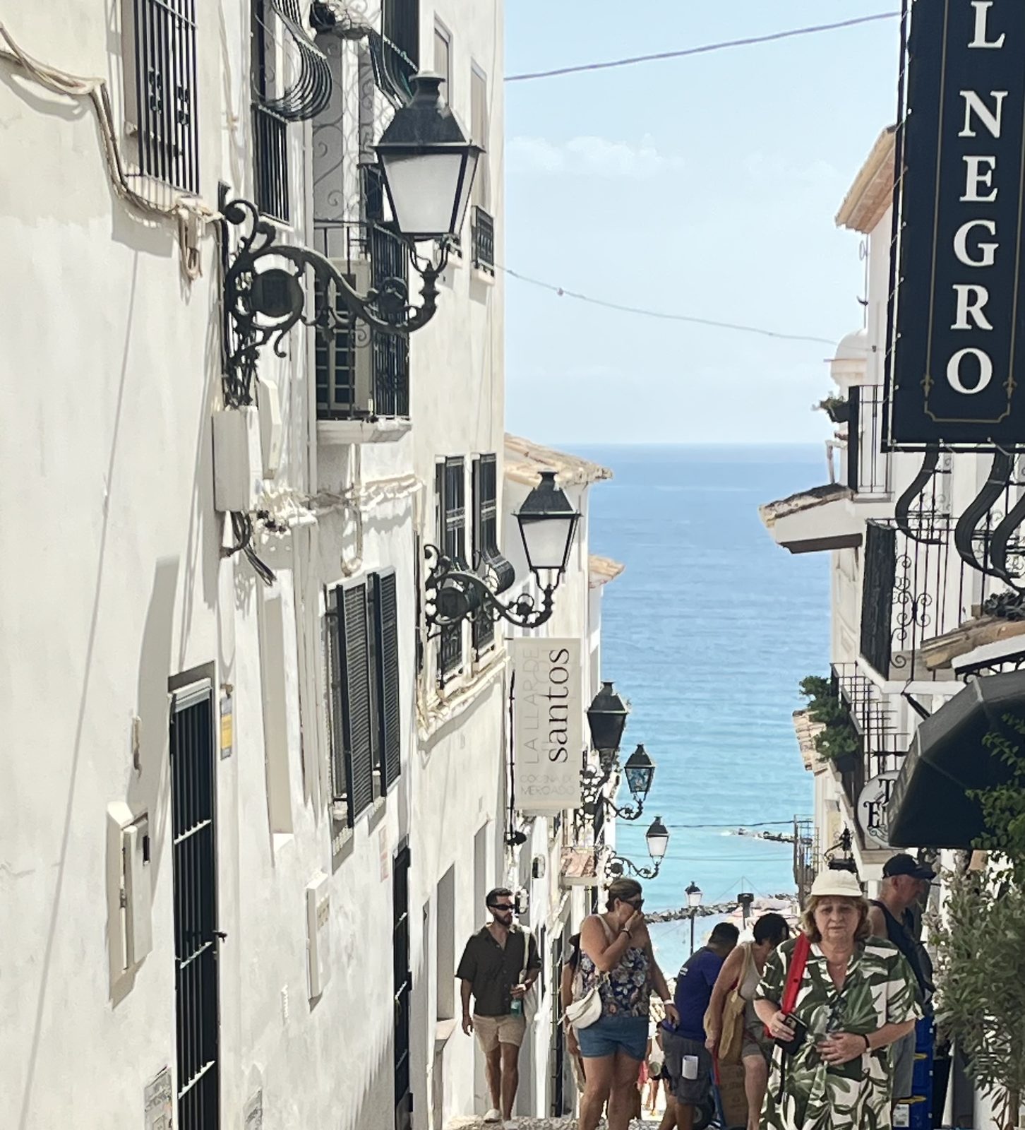 A steep cobbled street in Altea old town running down toward the Mediterranean, lined with wrought-iron lamps and white houses