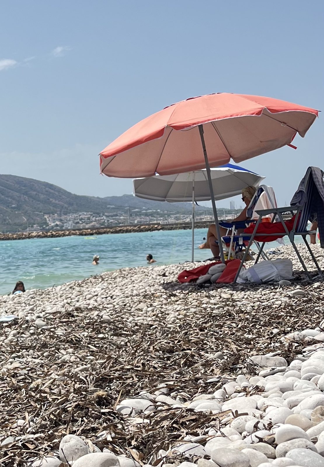 Altea's white pebble beach with a bank of dried seagrass along the waterline, turquoise water and the Serra Gelada headland beyond