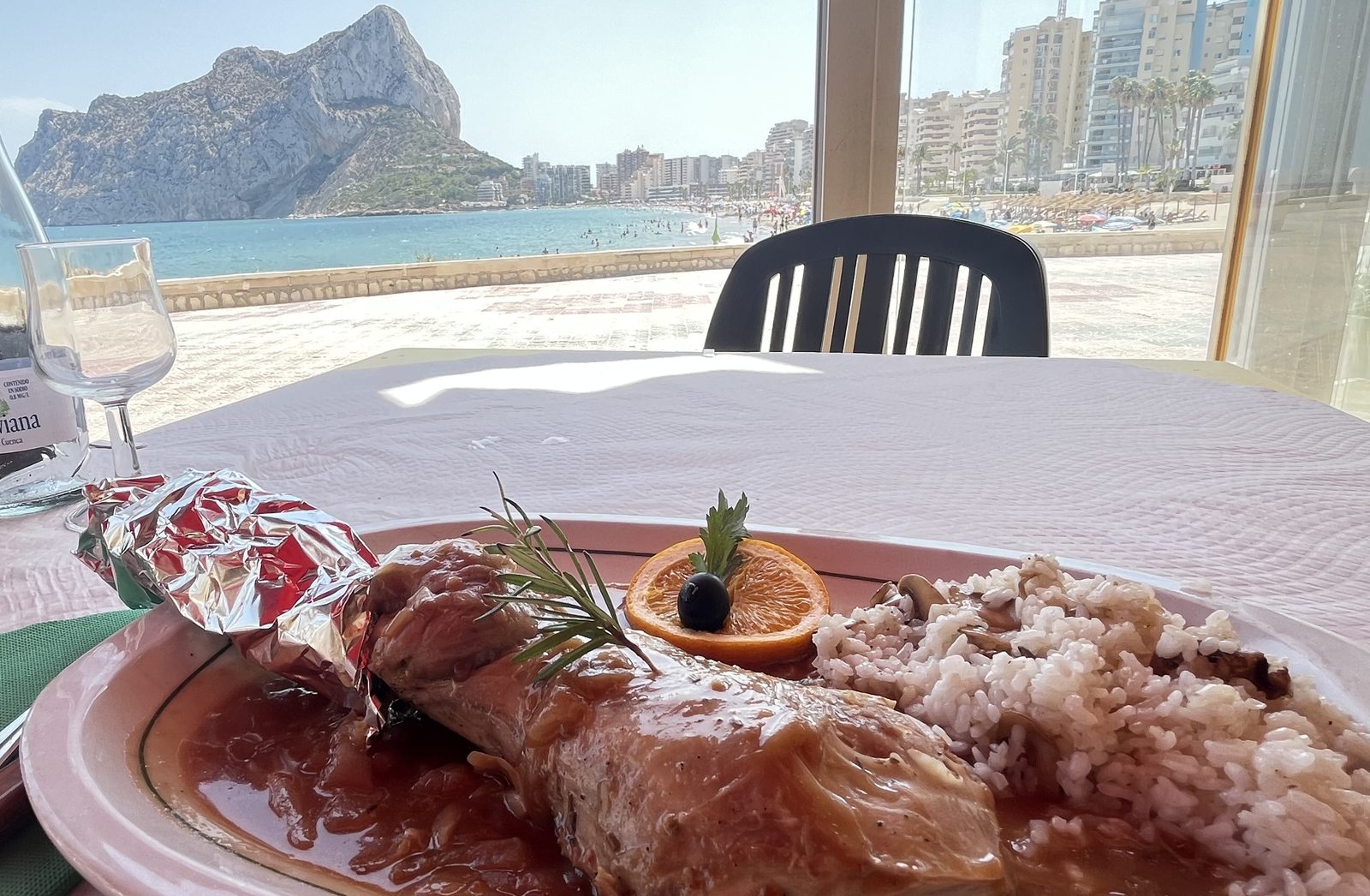 A menu del dia main course on a seafront restaurant table in Calpe, with the Peñón de Ifach and the beach visible through the window