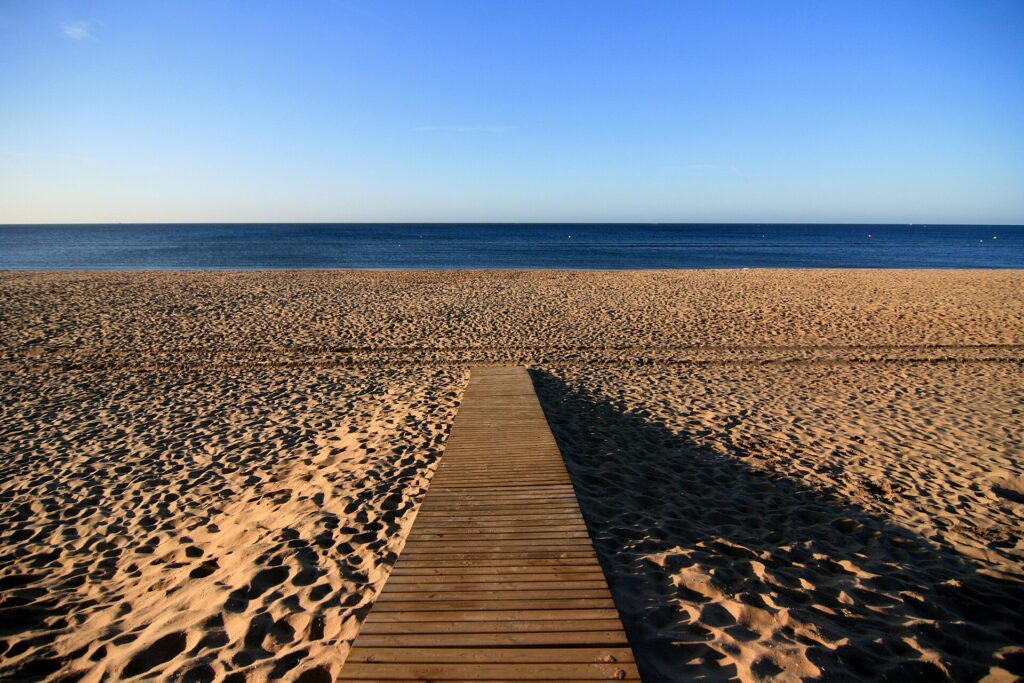 Wooden walkway leading across the wide sandy beach of Islantilla towards a calm sea and clear sky.