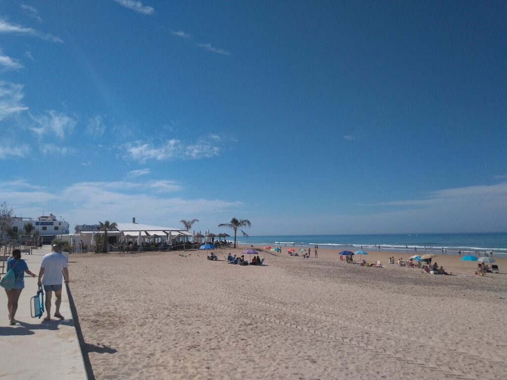 Playa de la Fontanilla in Conil de la Frontera, with promenade, beach bars and sunbathers on golden sand.