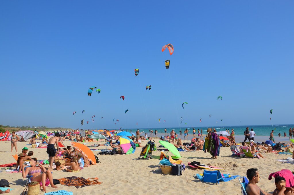 Busy sandy beach with dozens of kitesurfing kites in a blue sky at Playa de Valdevaqueros, Tarifa.