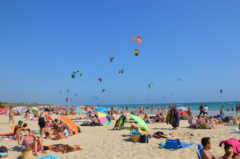 Busy sandy beach with dozens of kitesurfing kites in a blue sky at Playa de Valdevaqueros, Tarifa.