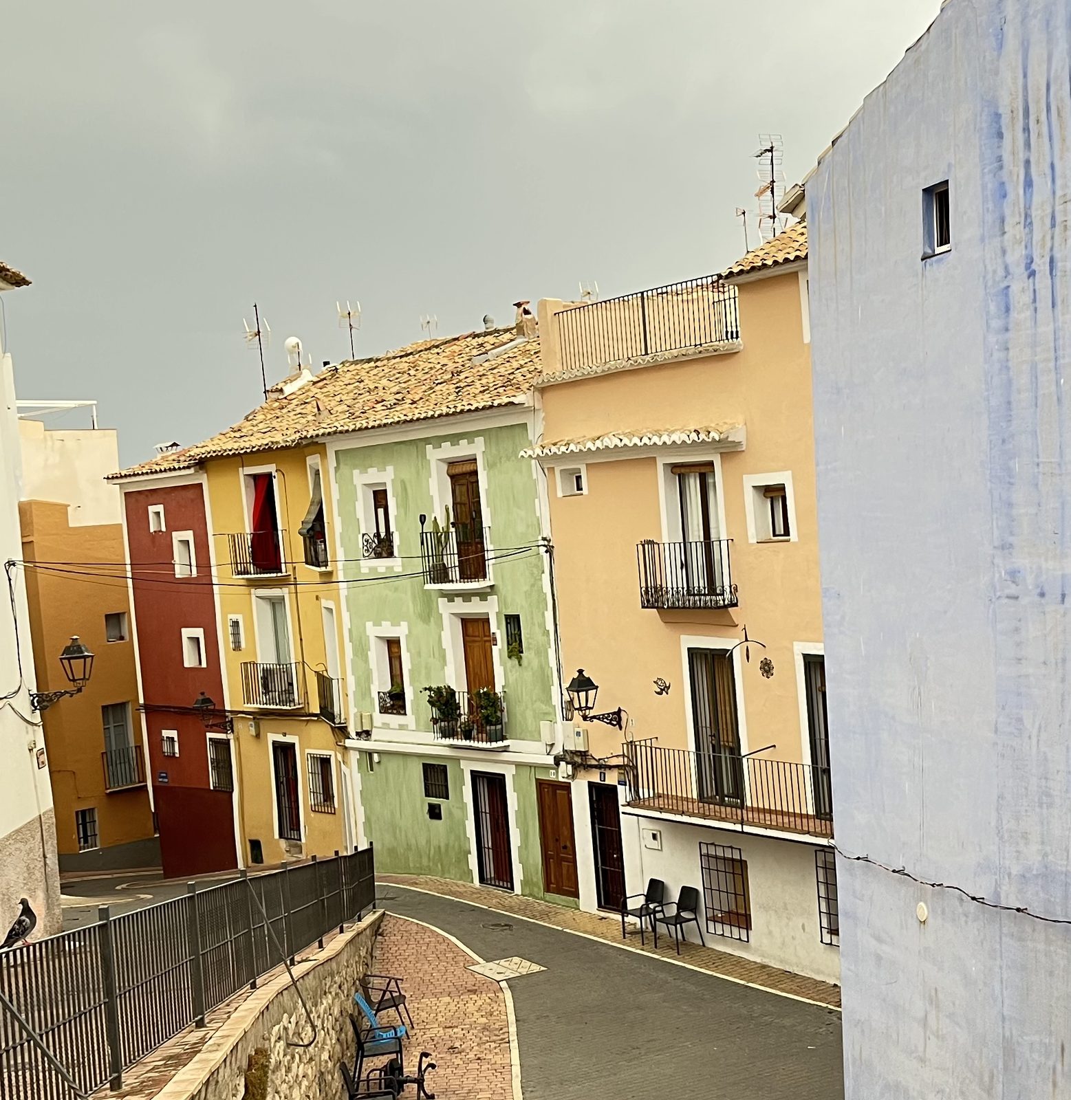 Rows of red, yellow, green and apricot houses in the old town of Villajoyosa seen from above, with tiled roofs and wrought-iron balconies