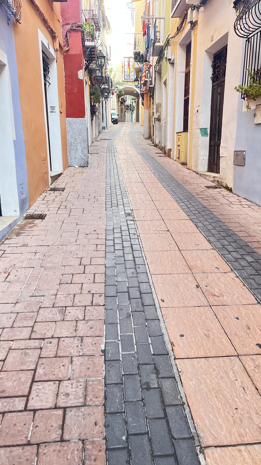 Narrow street in Villajoyosa old town lined with coloured houses, laundry and Valencian flags, with a low arch spanning the lane