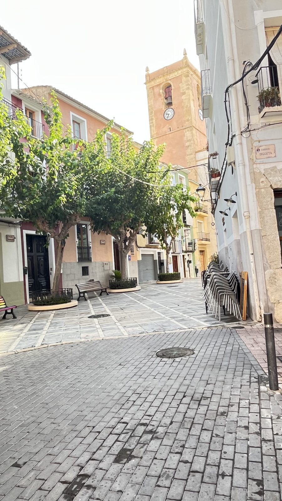 Trees and benches on a small square in Villajoyosa old town with the bell tower of the Asunción church behind